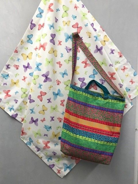 Bunte, gestreifte Schultertasche hängt vor einem Stoffhintergrund mit Schmetterlingsmuster.
