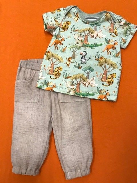 Baby-Outfit mit hellem T-Shirt mit Tiermuster und beiger Hose auf orangefarbenem Hintergrund