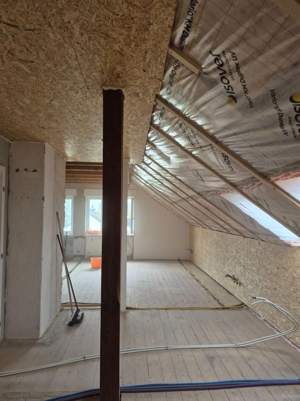 Im Bau befindlicher Dachboden mit schrägem, isoliertem Dach, freiliegenden Balken und einem zentralen Stützpfeiler.