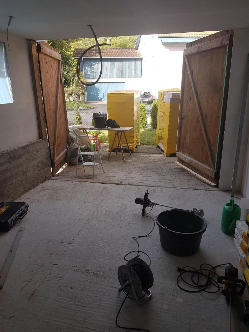 Offene Garage mit Werkzeug und Kabeln auf dem Boden, gelben Schränken im hinteren Bereich und grossen, zum Tageslicht offenen Türen.