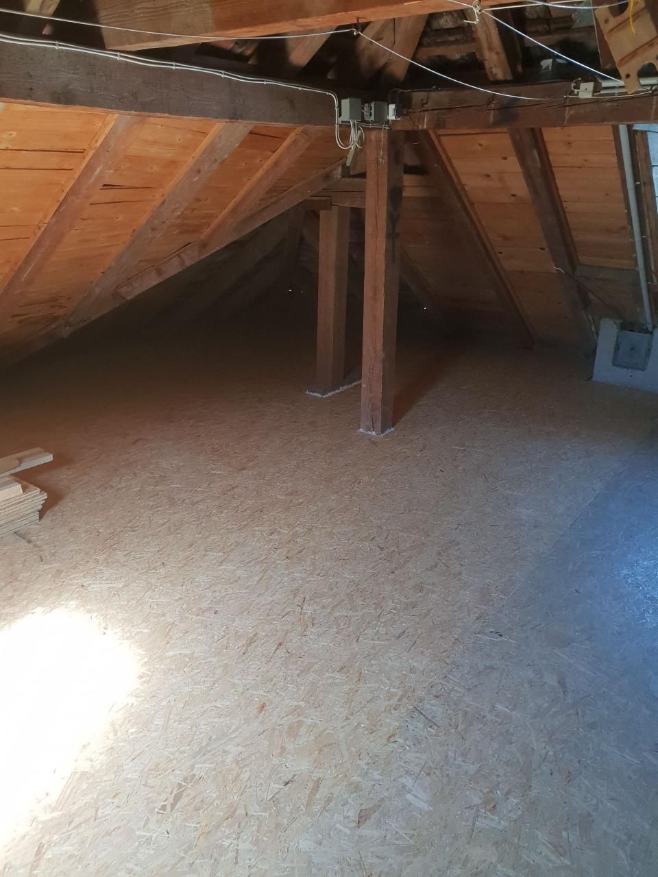 Dachboden mit freiliegenden Holzsparren, zentralen Stützbalken und einer schrägen Decke über Sperrholzboden