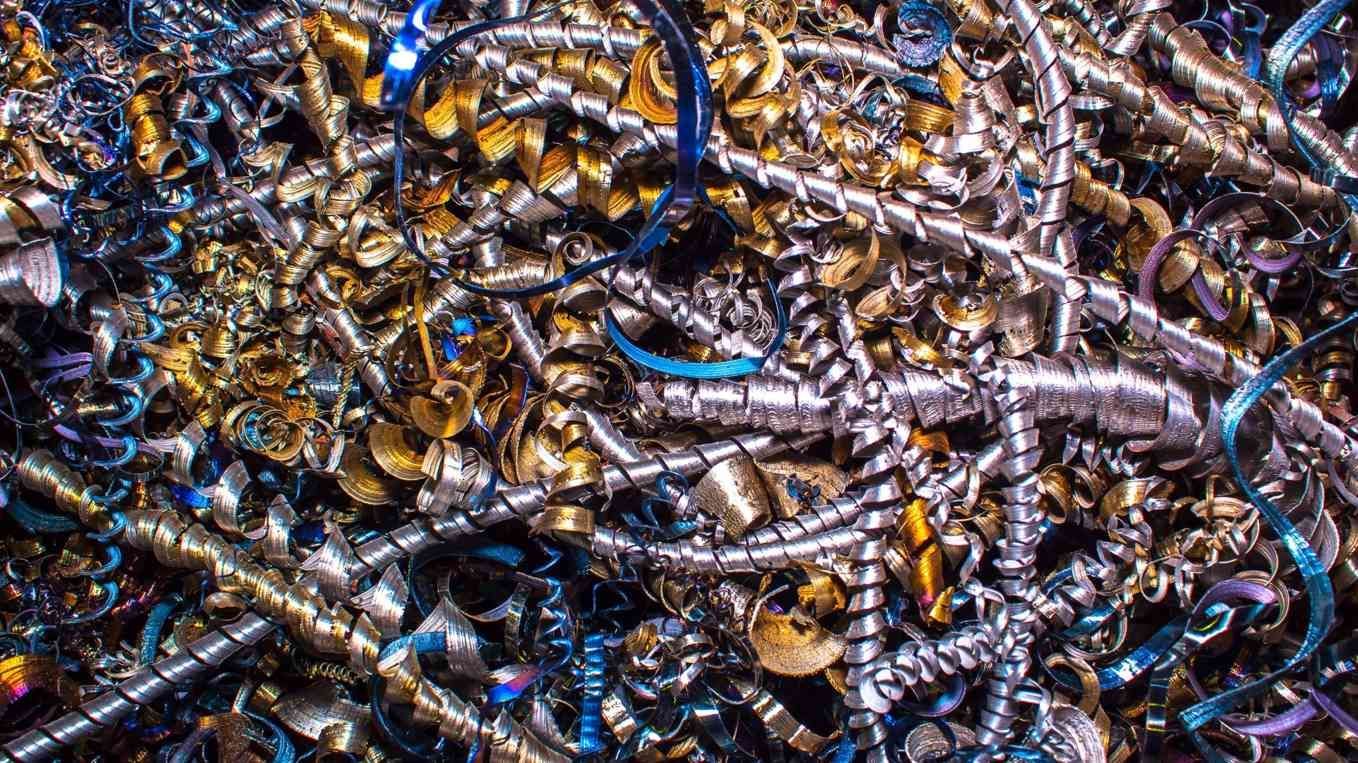 Montón de restos metálicos enredados y bobinas de alambre en tonos plateados, dorados y azules.