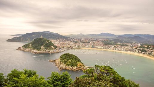 Bahía costera con islotes verdes, playa de arena y una ciudad a lo largo de la costa bajo un cielo brumoso.