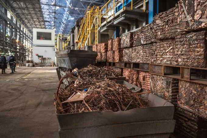 Almacén industrial con fardos de chatarra de cobre apilados y una gran pila de chatarra metálica en primer plano.