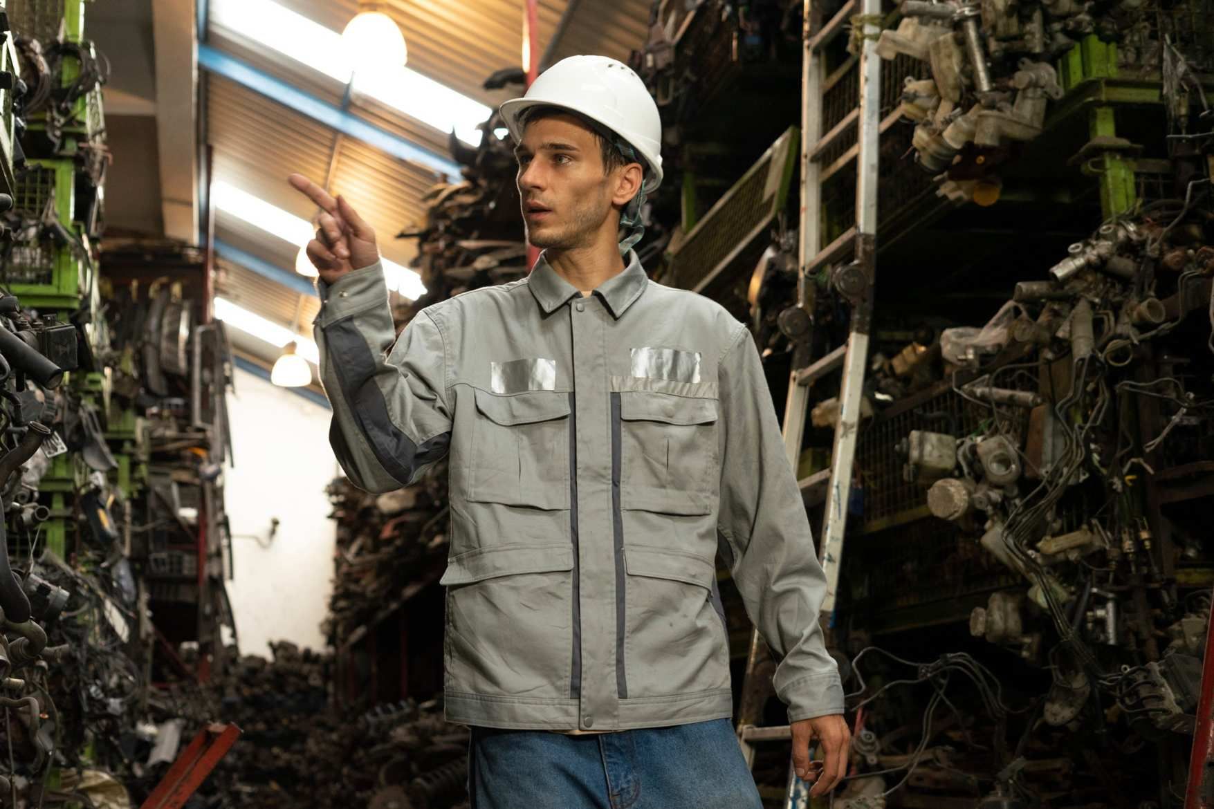 Un trabajador con casco y chaqueta gris se encuentra en una planta industrial, sosteniendo una luminaria.