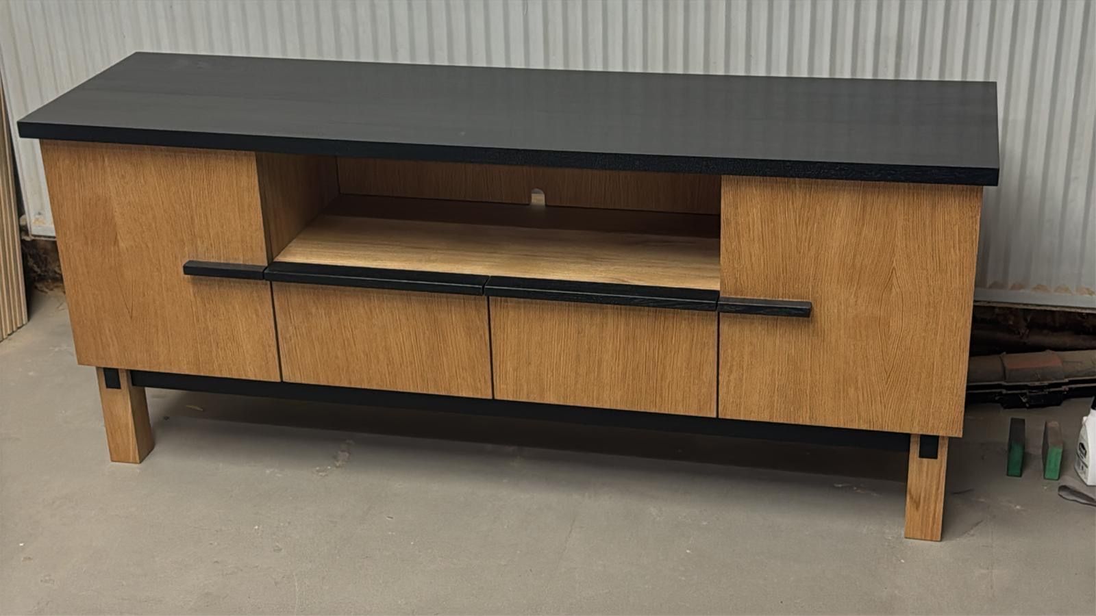 TV-Ständer aus Holz mit schwarzer Platte, hellbraunen Schränken und offenem Regal.