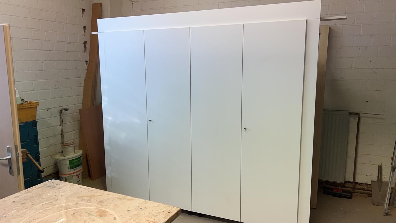 Weißer Schrank mit vier Türen in einer Werkstatt.