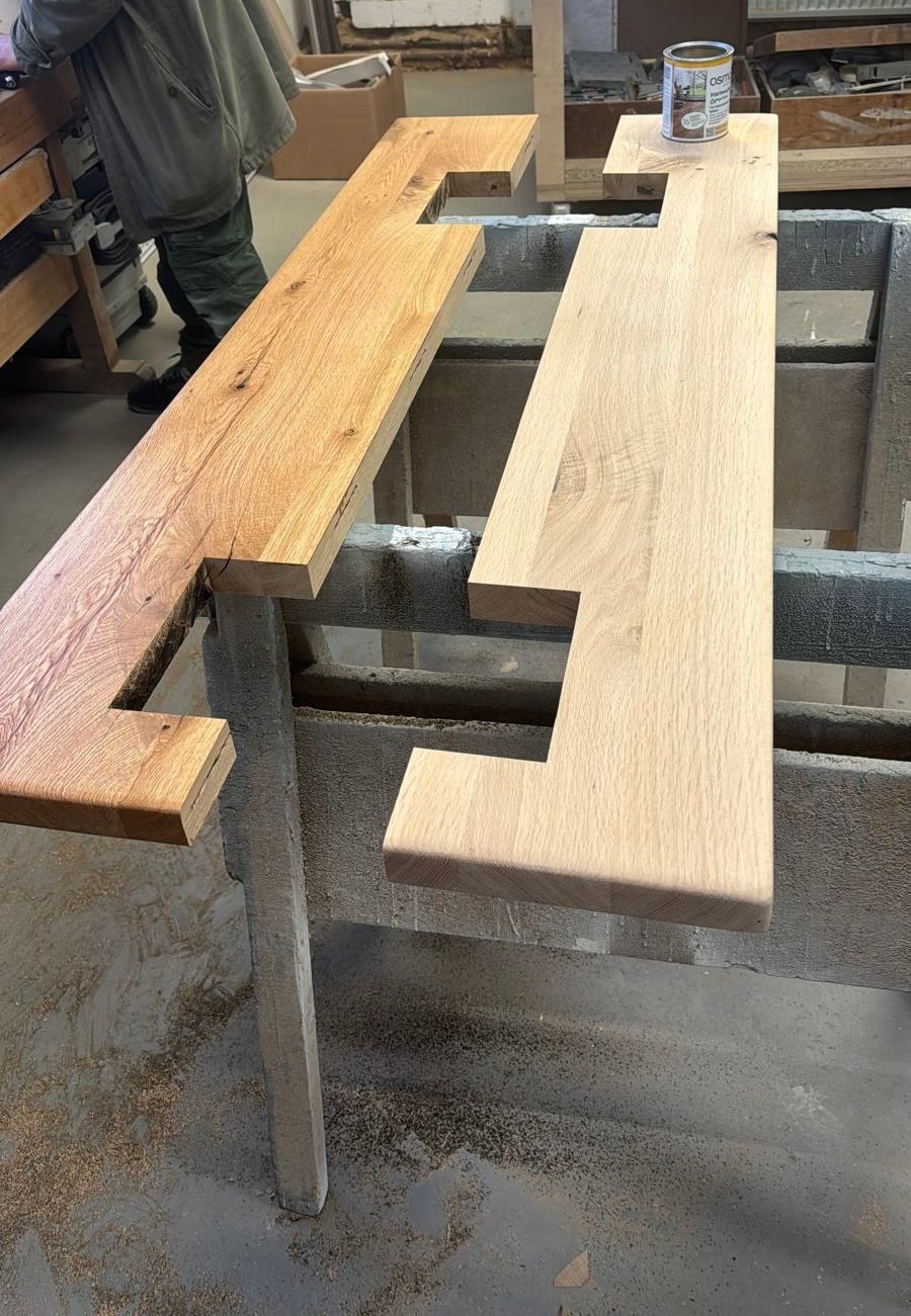 Eine Holztreppe lehnt an einer Wand in einer Werkstatt. Helles Holz, offenes Design und sichtbare Stufen.