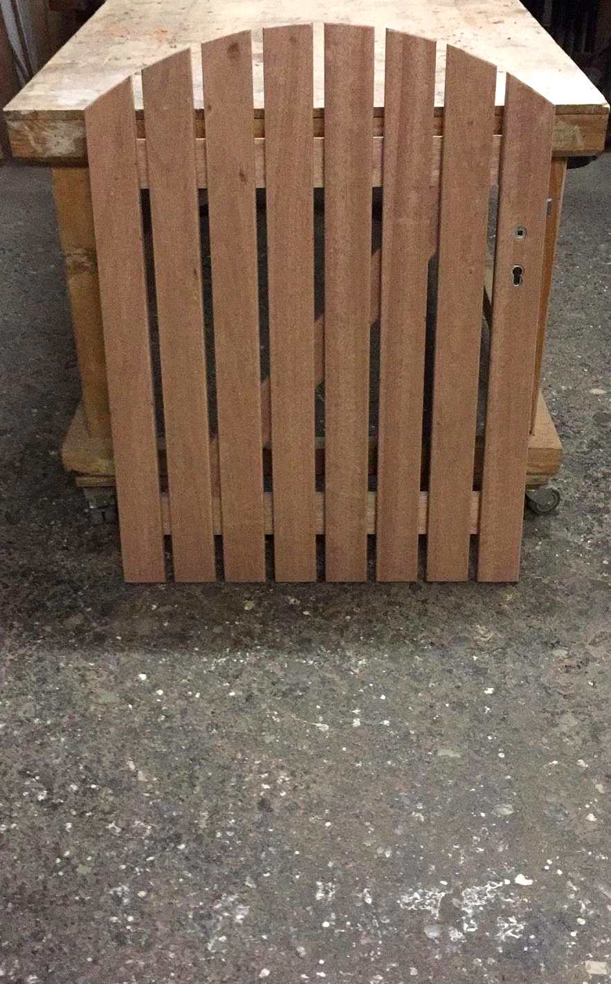 Holztor mit senkrechten Brettern und gewölbtem Oberteil, auf einer Werkbank. Braunes Holz mit sichtbarer Maserung.