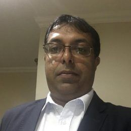 A man wearing glasses and a suit is taking a selfie.