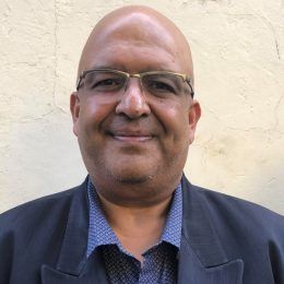 A bald man wearing glasses and a suit is smiling for the camera.