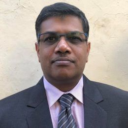 A man in a suit and tie is standing in front of a wall.