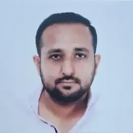 A man with a beard is wearing a white shirt and looking at the camera.
