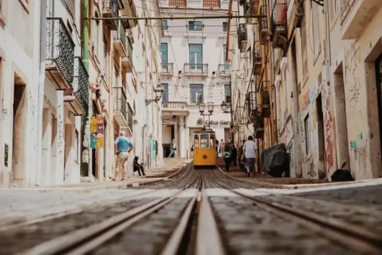 A yellow trolley is going down a narrow street in a city.