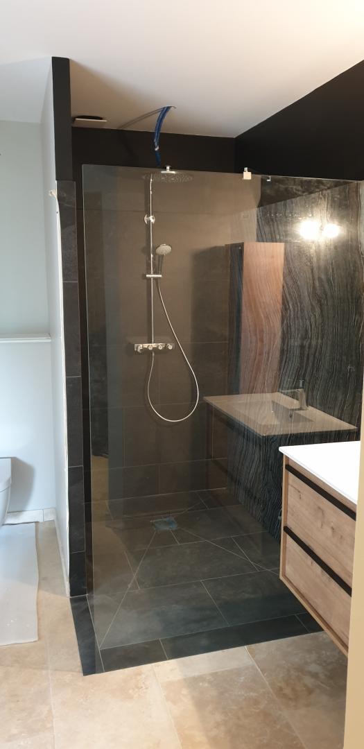 Douche et carrelage sombre derrière une paroi vitrée