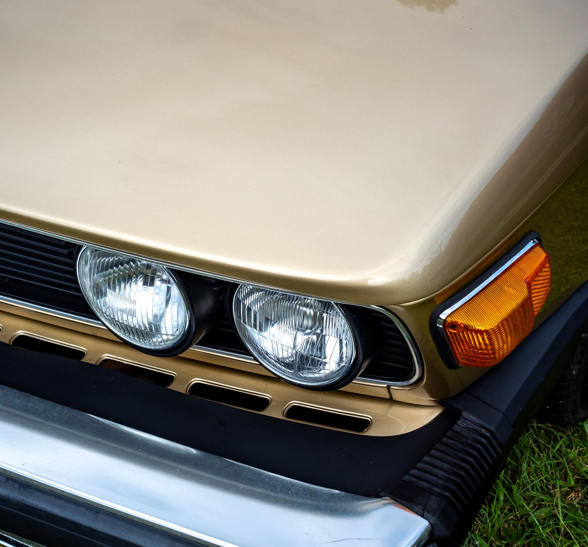 Face avant dorée d'une voiture classique avec phares et clignotants latéraux orange.