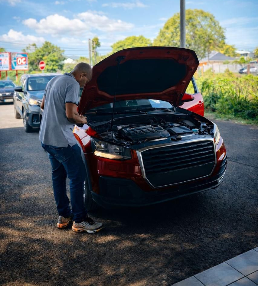 Une personne se tient près d'une voiture, capot ouvert, et examine le moteur sur un parking extérieur.
