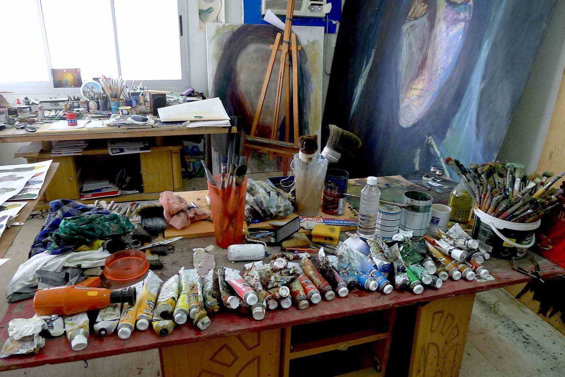 Una mesa con muchos tubos de pintura y pinceles encima.