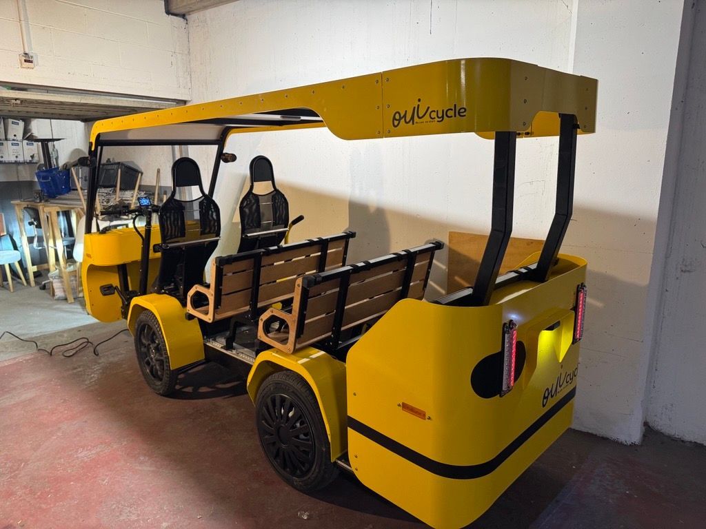Chariot utilitaire électrique jaune stationné dans un garage, avec un auvent noir et des sièges ouverts.