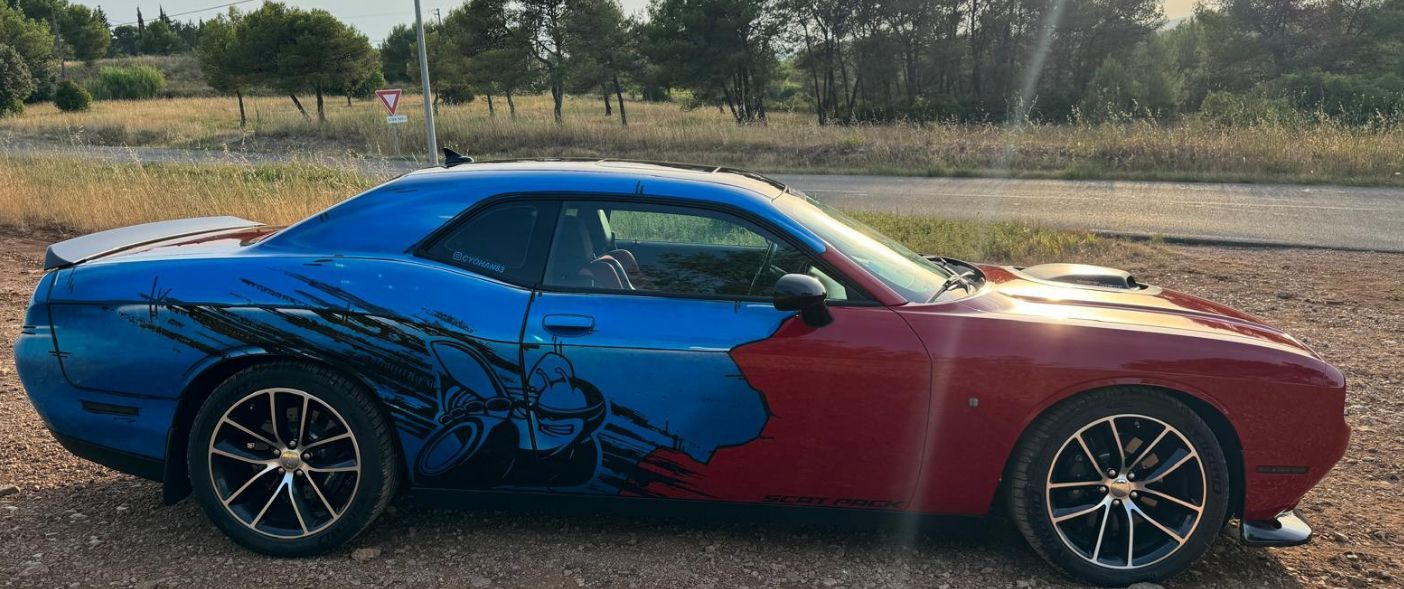 Voiture de sport personnalisée bleue et rouge garée sur un chemin de gravier avec des arbres en arrière-plan.