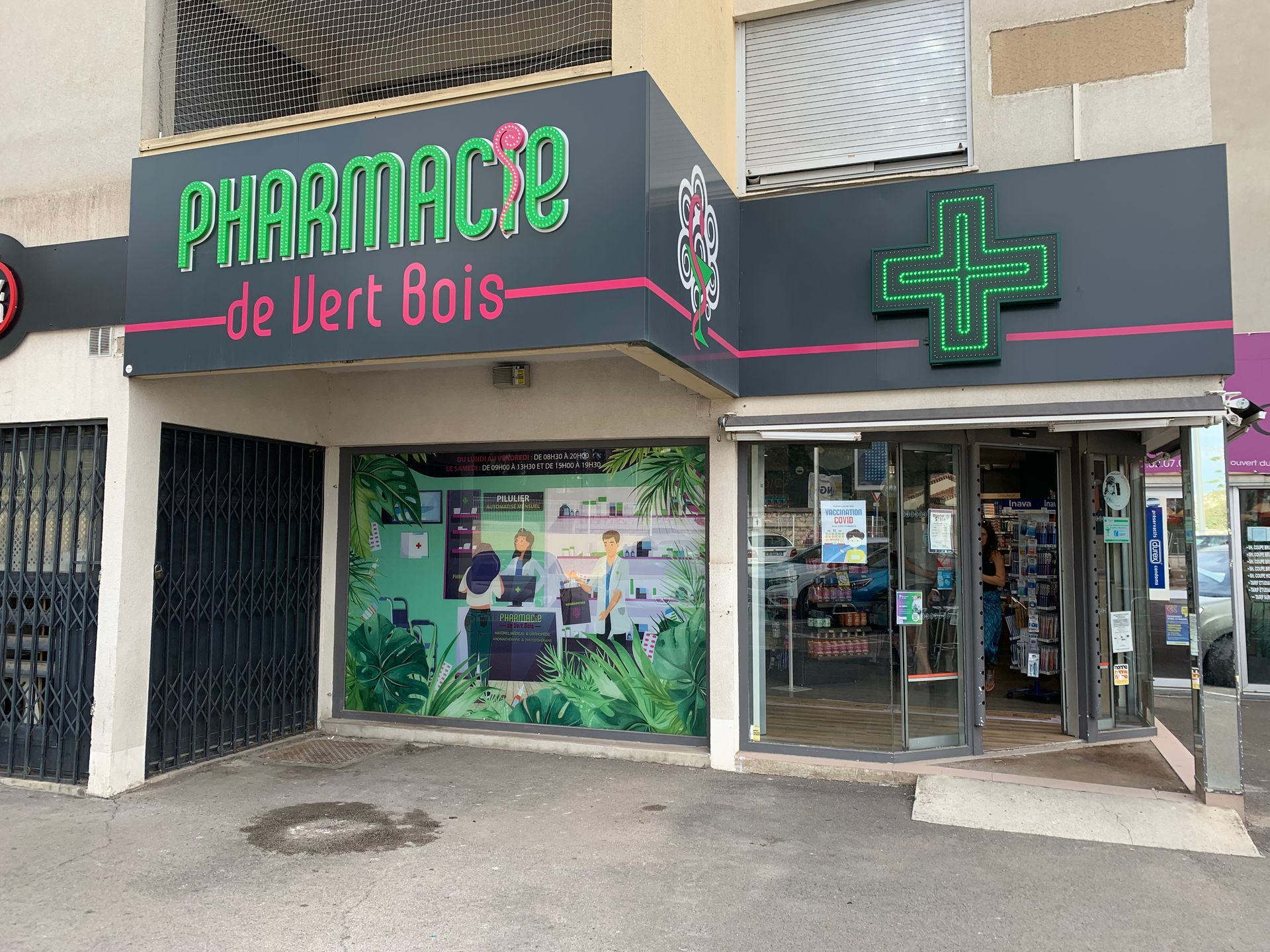 Façade de pharmacie avec une enseigne en forme de croix verte.