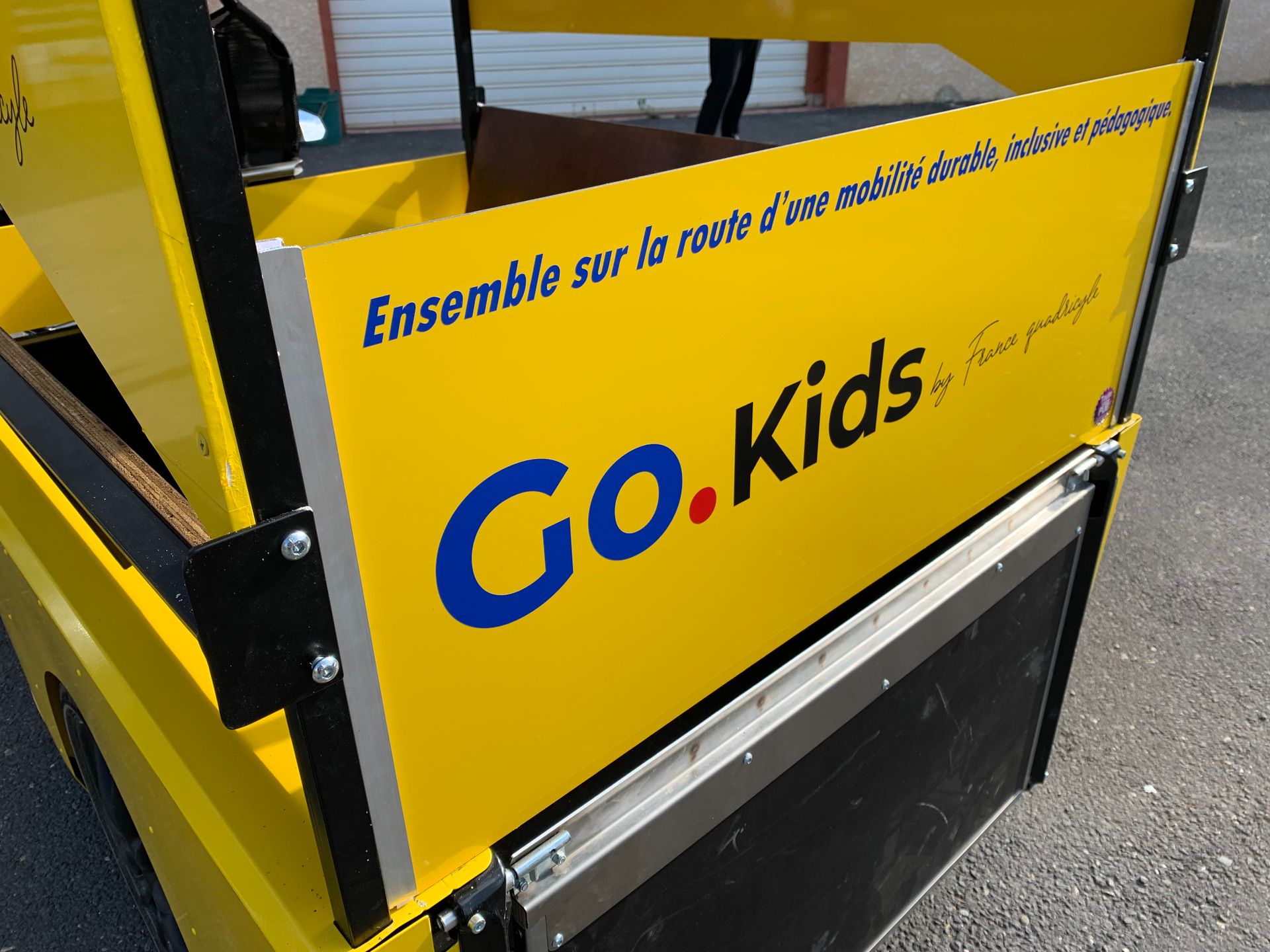 Chariot jaune Go-Kids avec inscription en français, stationné sur le trottoir à l'extérieur.