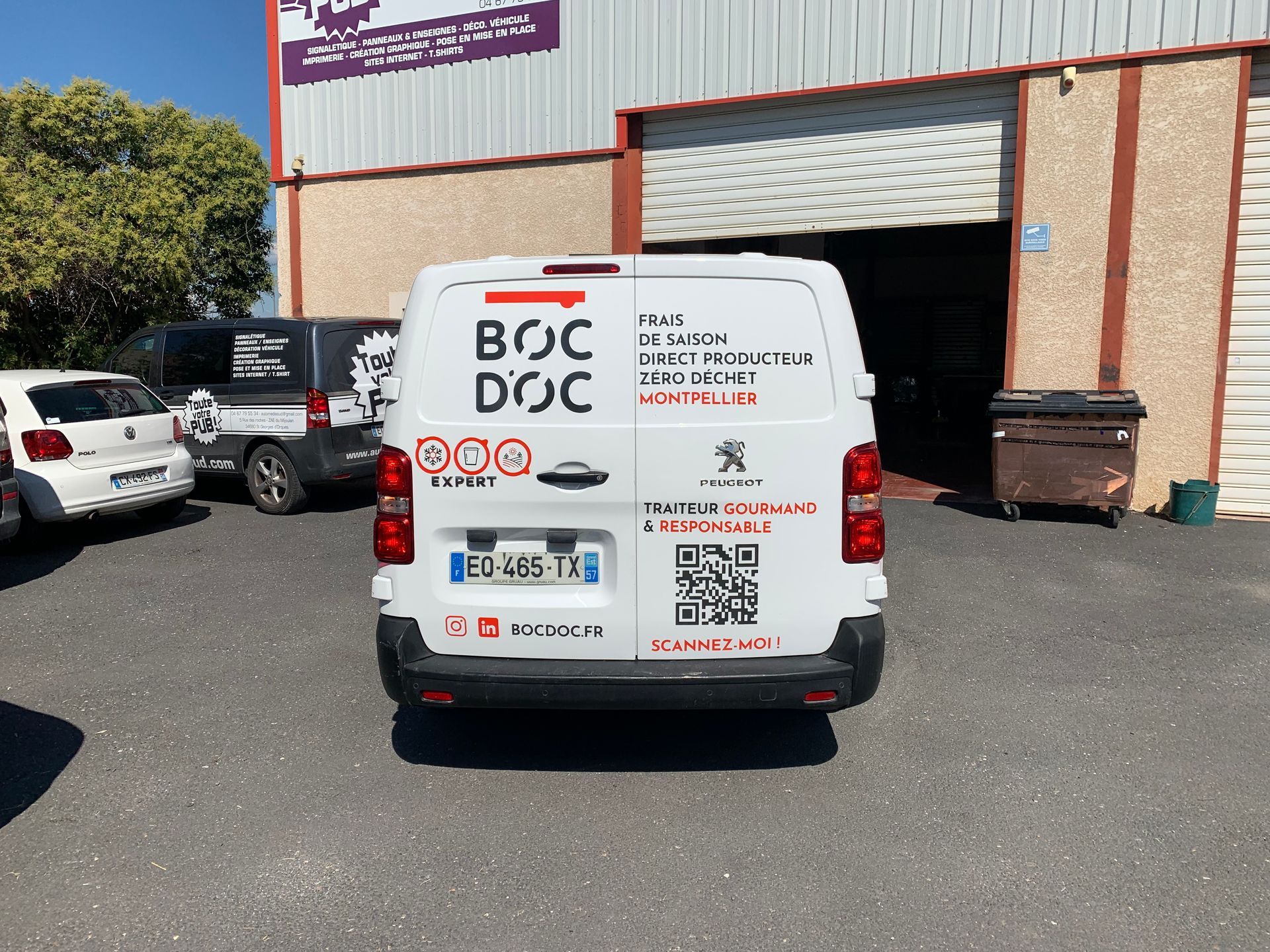 Camionnette de livraison blanche portant la marque BOC DOC, stationnée devant un quai de chargement d'entrepôt.