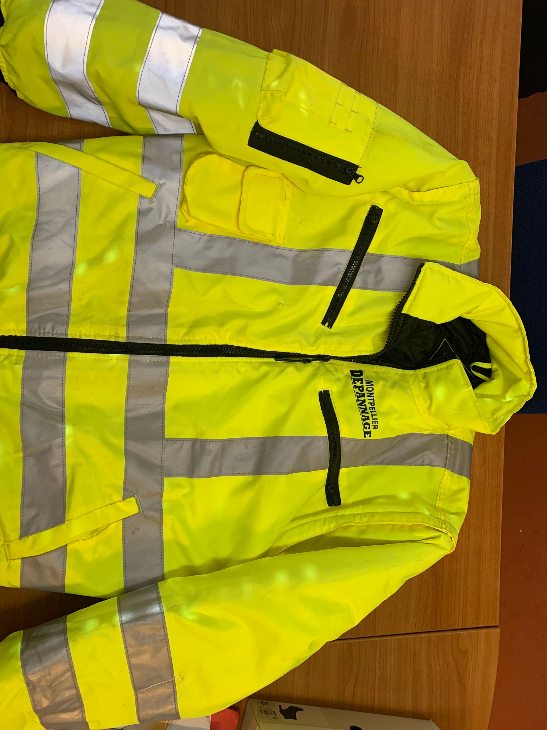 Gilet jaune haute visibilité avec bandes réfléchissantes accroché à un mur en bois.