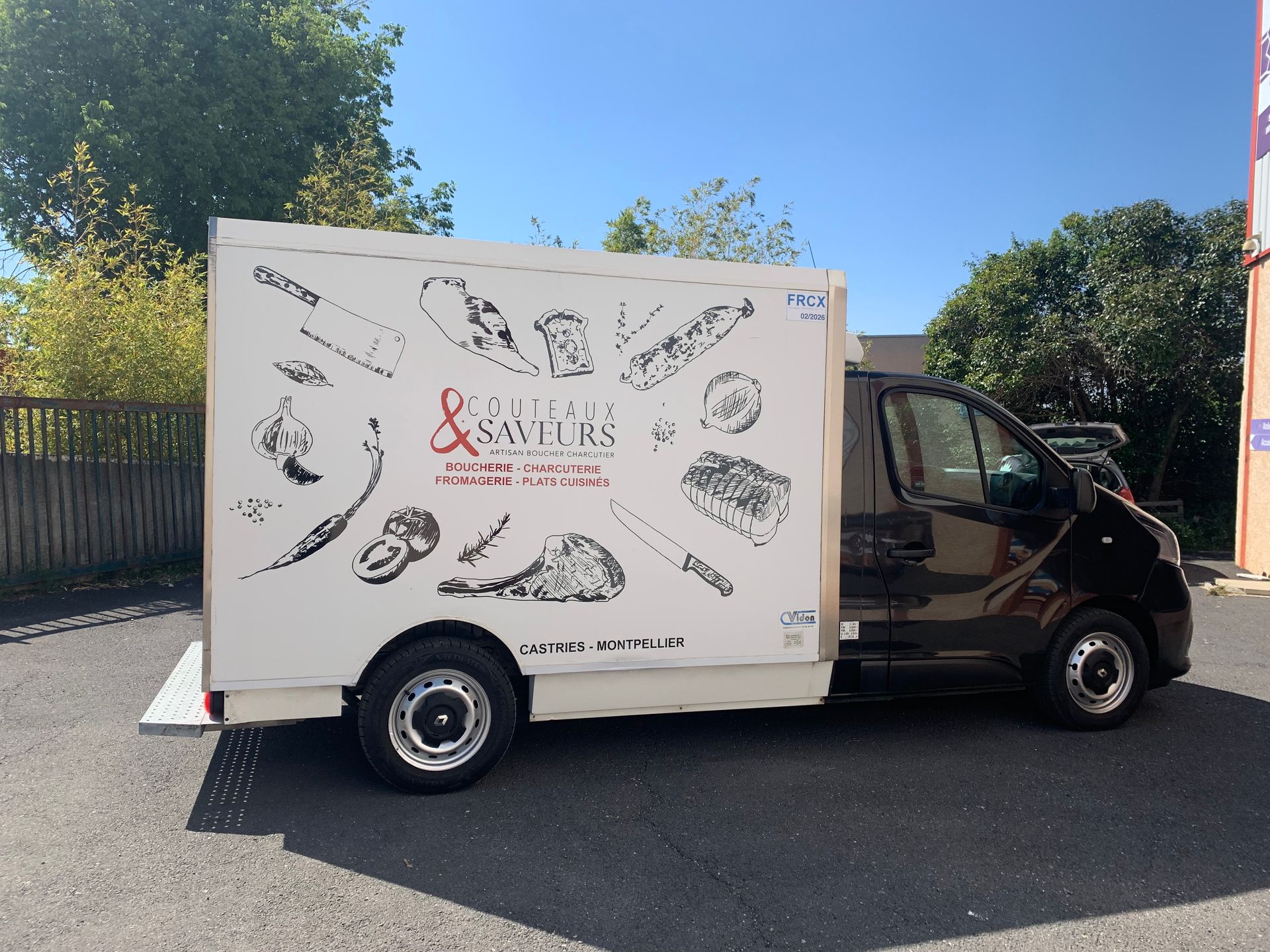 Camionnette de livraison blanche Savorys garée en plein air dans une rue ensoleillée, panneau latéral recouvert d'illustrations de nourriture.