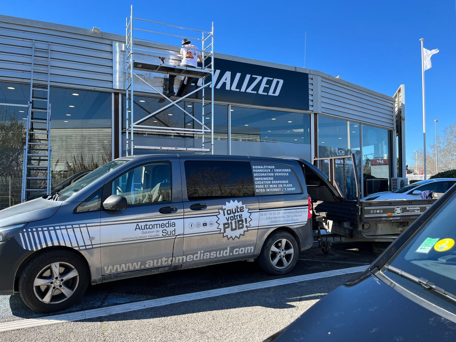 Une camionnette grise de l'entreprise est garée devant un magasin.