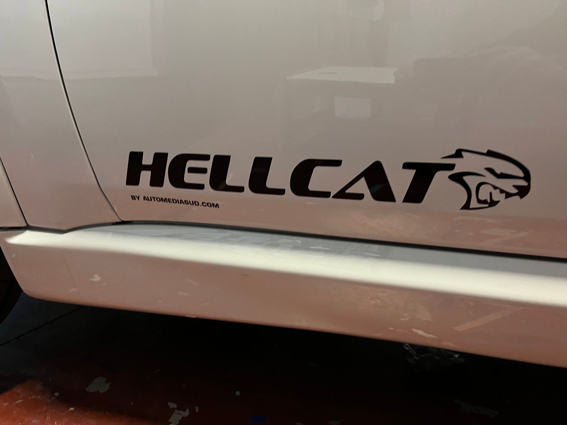Portière de voiture blanche avec un autocollant noir HELLCAT et le logo Hellcat au-dessus d'un bas de caisse.