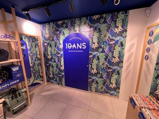 Porte bleue  10 ANS dans une petite boutique avec papier peint à motifs végétaux et étagères d'exposition.
