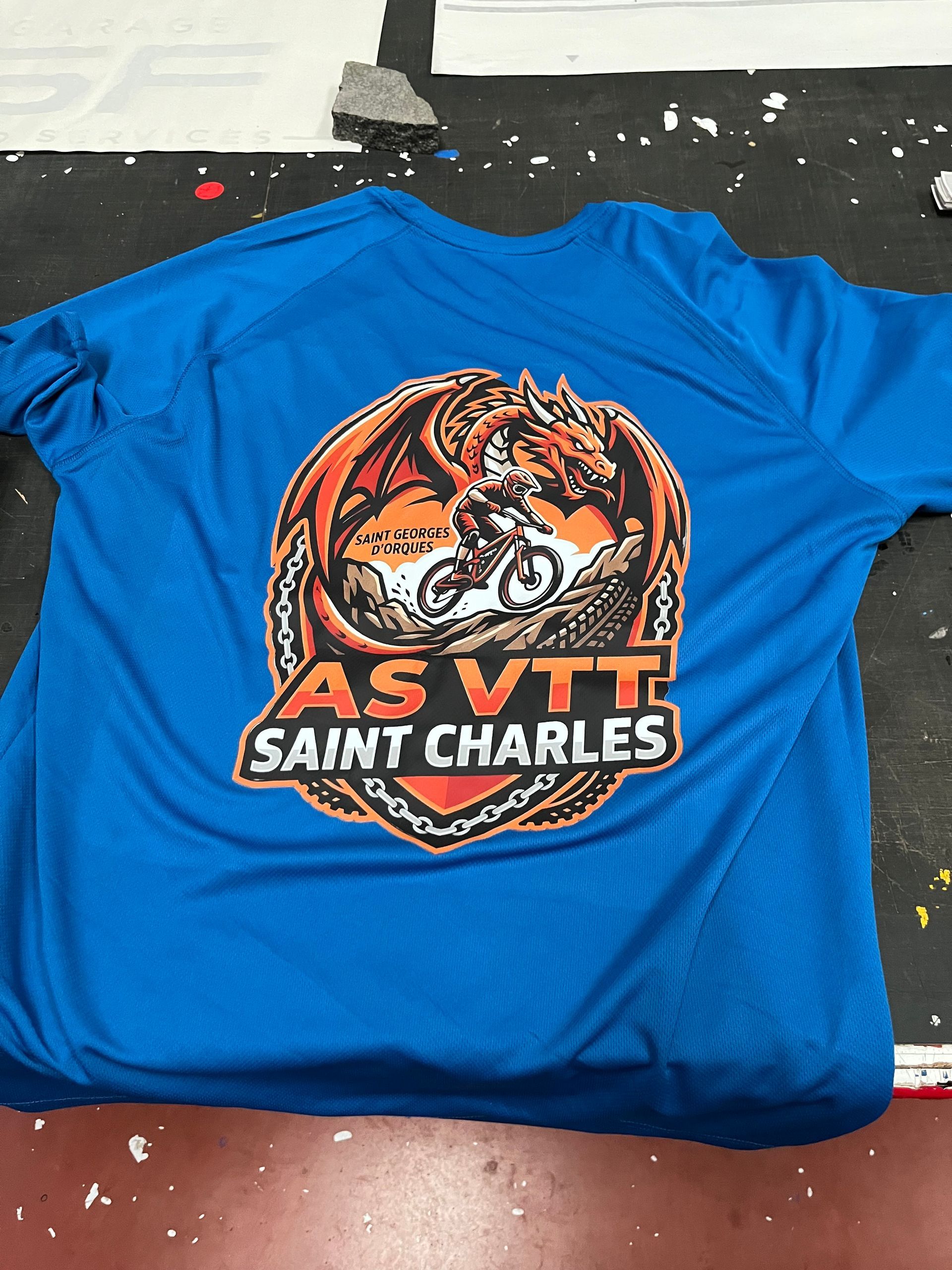 T-shirt bleu avec le logo de VTT de Saint Charles AS sur une table.
