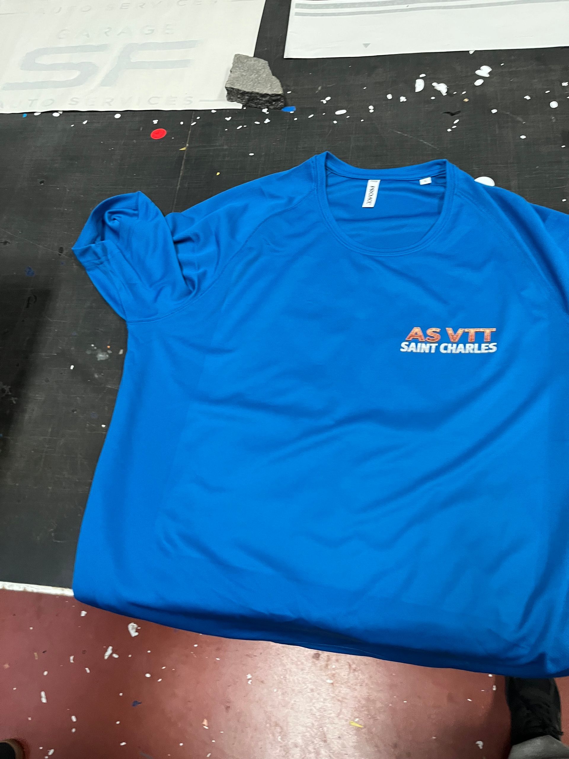 Un t-shirt bleu avec un petit logo, posé sur un tapis de sol foncé.