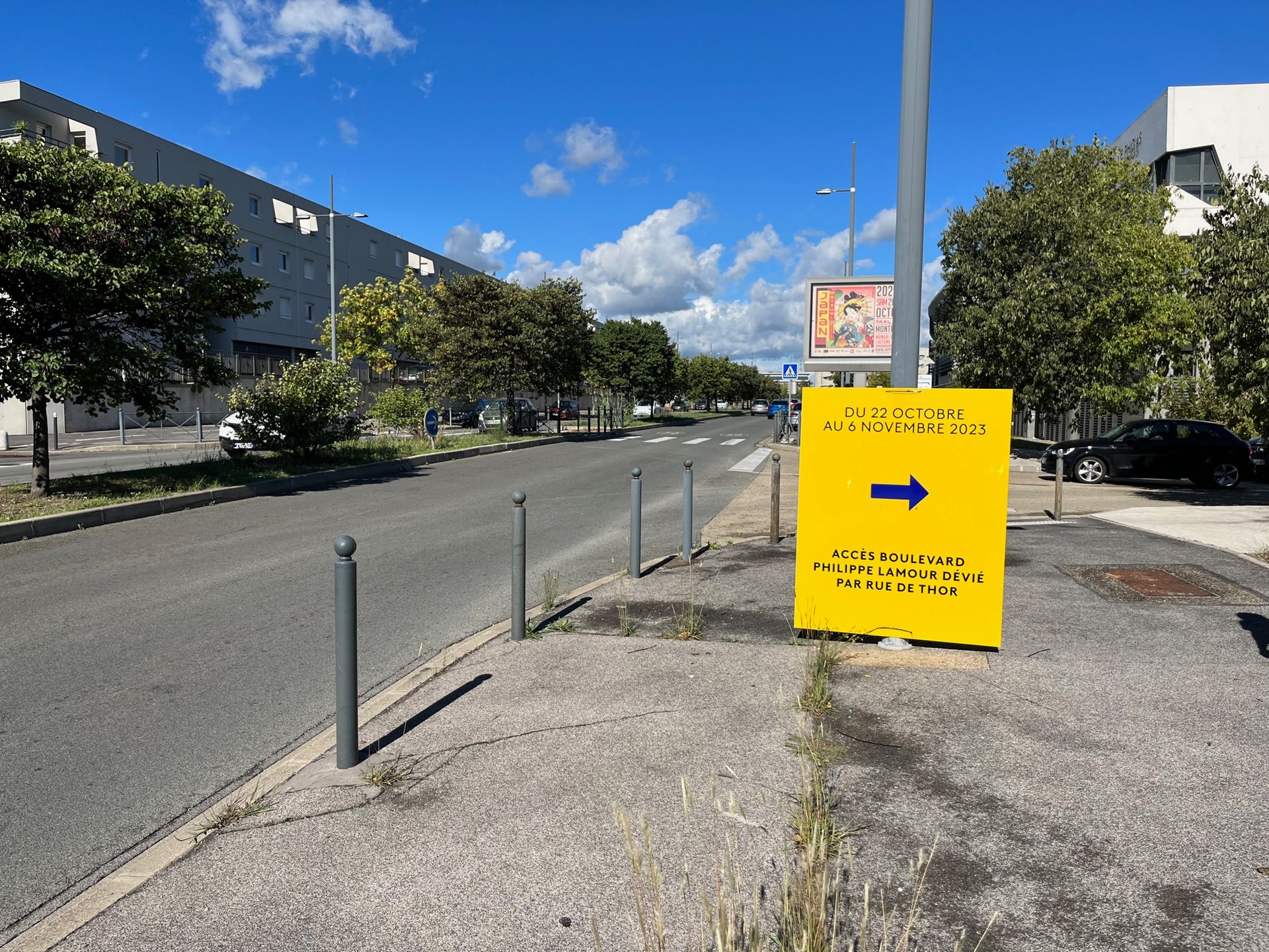 Panneau directionnel jaune vif au bord d'une rue, pointant vers la droite sous un ciel bleu.