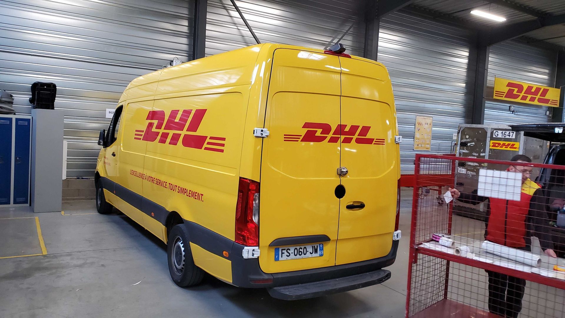 Camionnette de livraison jaune DHL stationnée dans une zone de chargement d'entrepôt.
