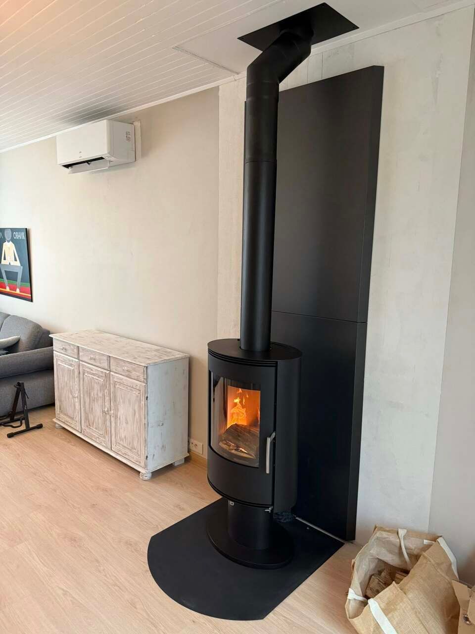 Poêle à bois noir avec un feu allumé équipé d'un conduit de cheminée noir et d'une protection murale.