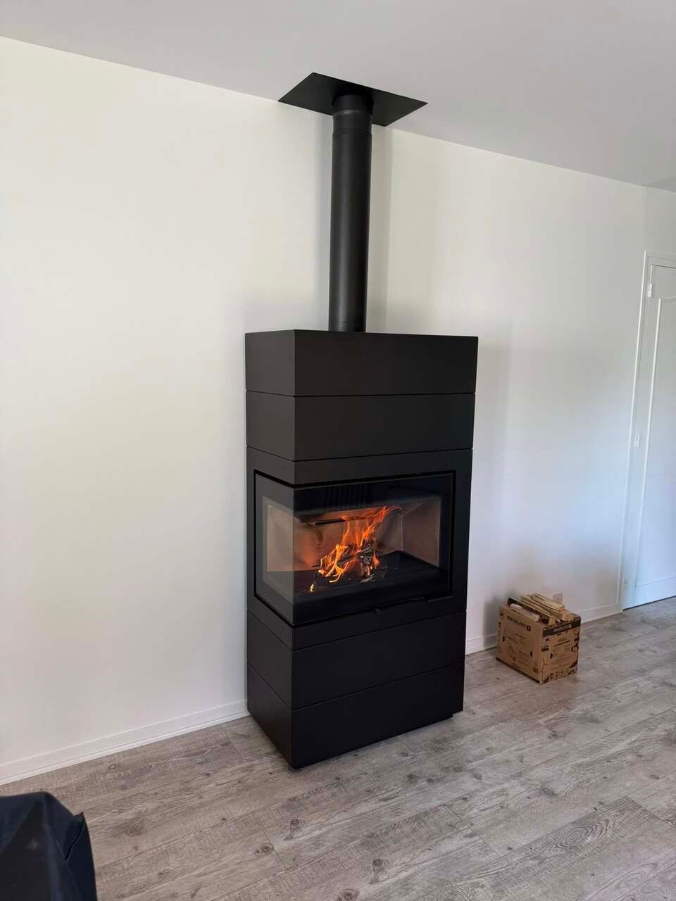 Poêle moderne noir avec flammes allumées et conduit noir sur un mur blanc.