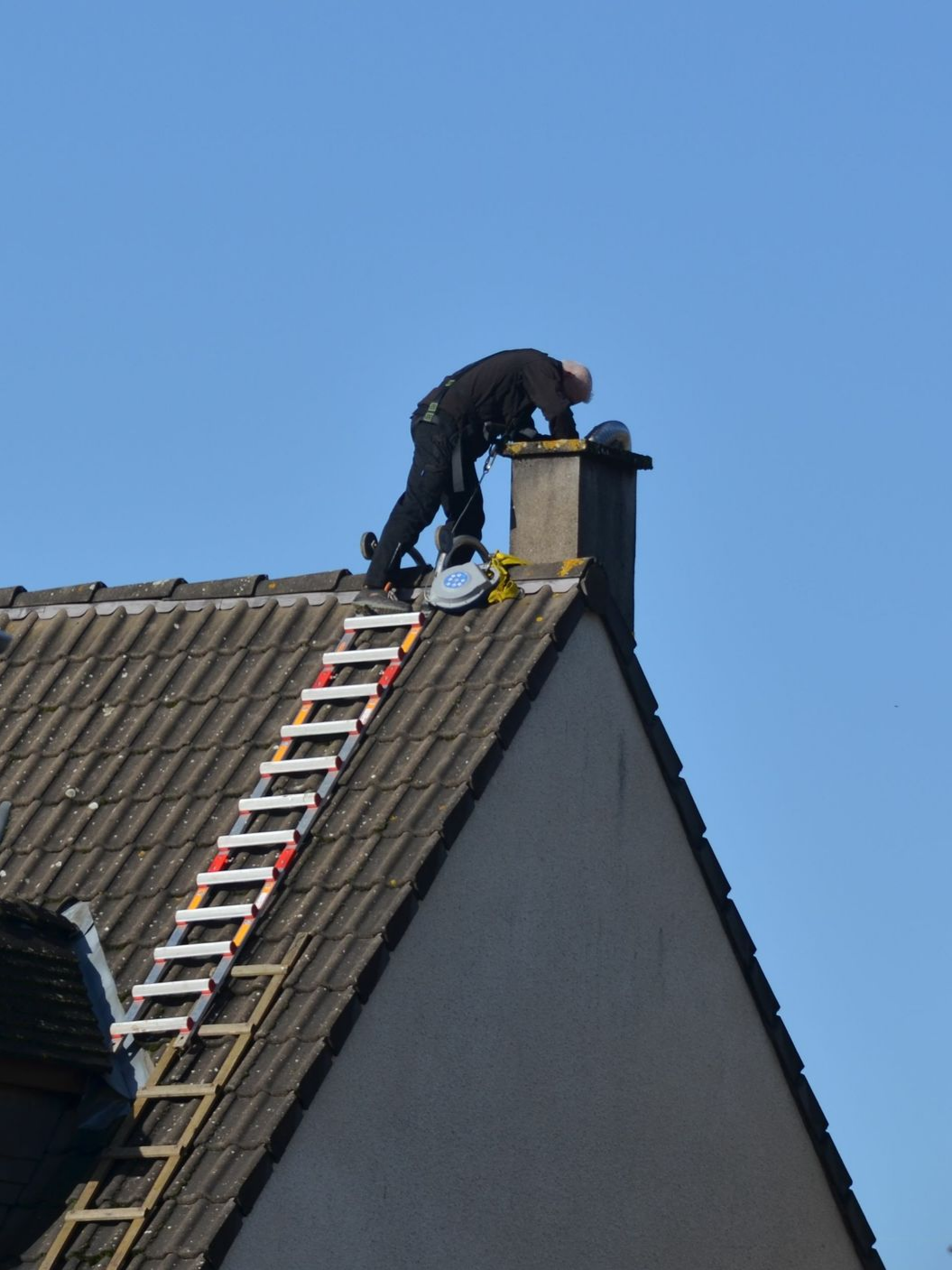 Un artisan se trouve sur un toit, penché au-dessus d'une cheminée.
