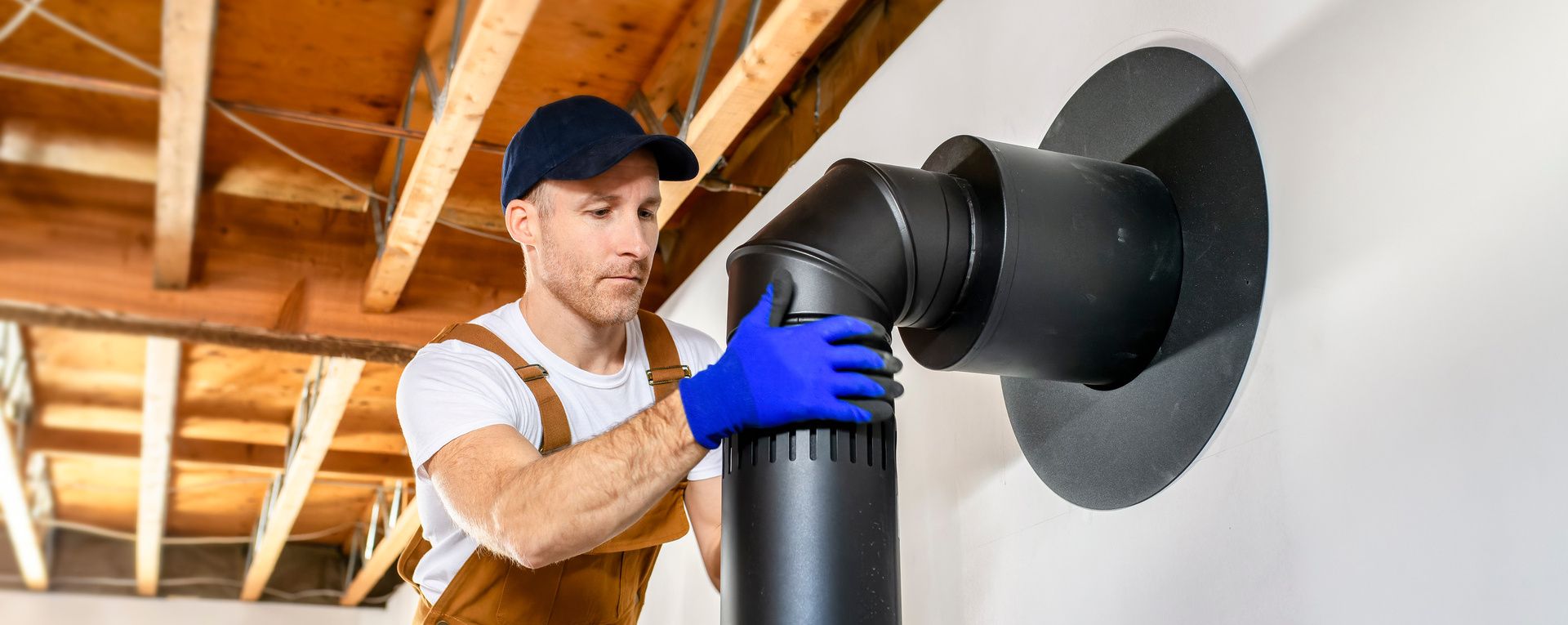 Artisan qui installe un tubage contre un mur blanc, sous un plafond en bois.