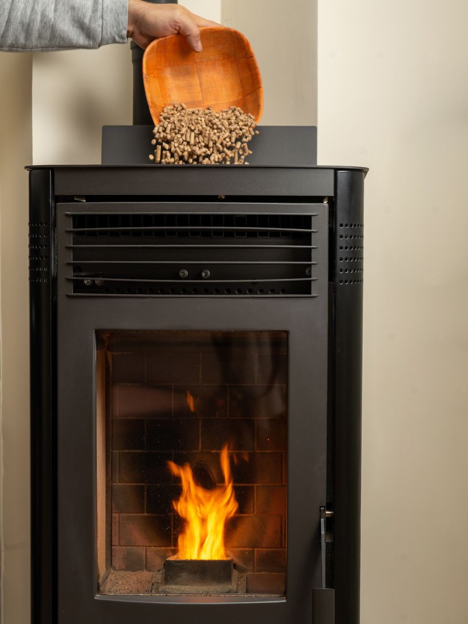 Une personne verse des granulés de bois dans un poêle à granulés allumé.