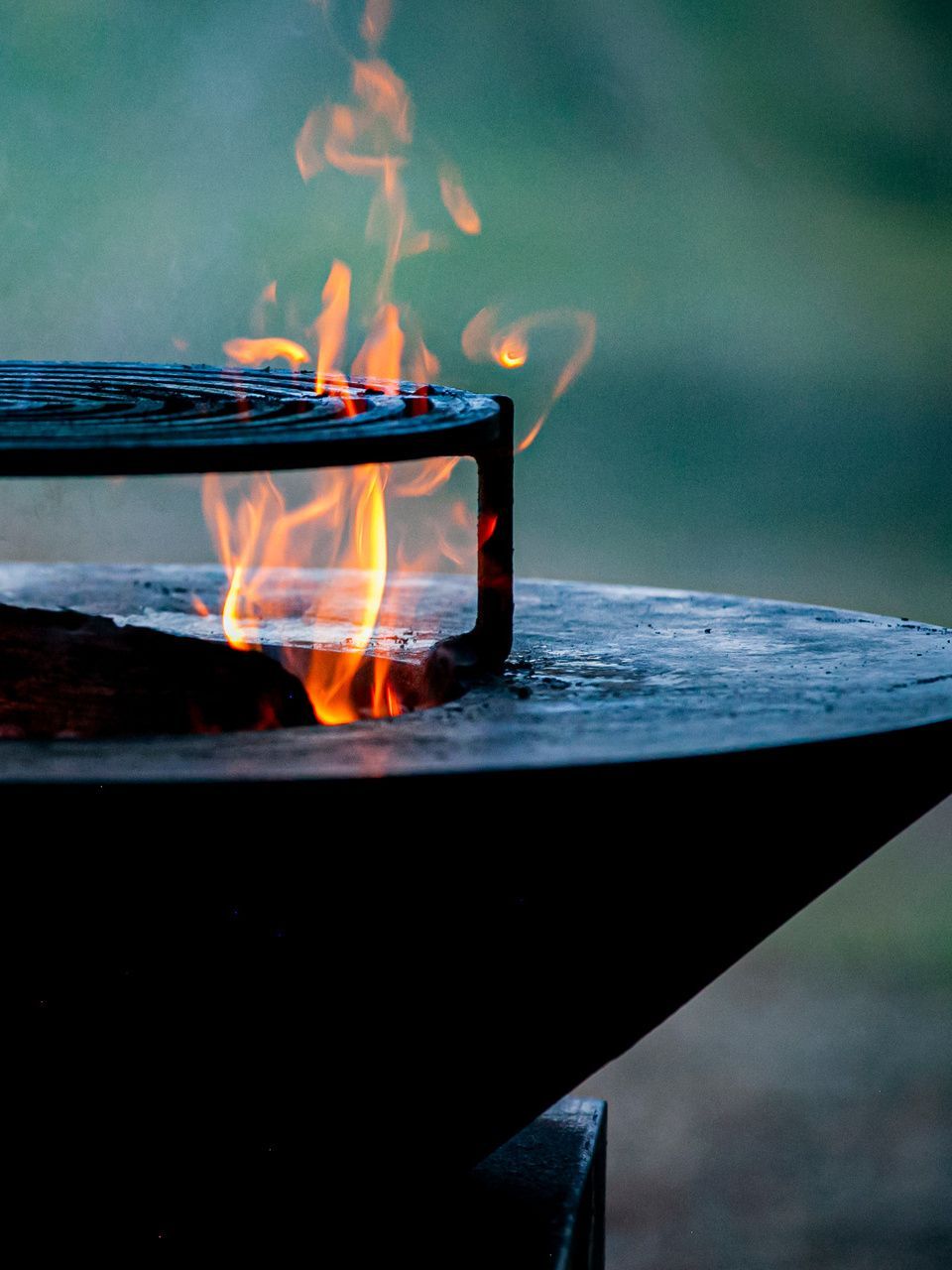 Feu dans un brasero en métal noir, avec une grille de barbecue par-dessus.