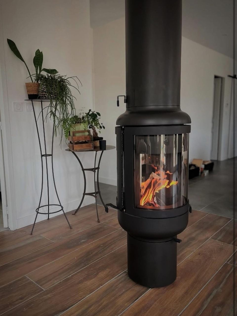 Un poêle à bois cylindrique noir avec une porte vitrée.