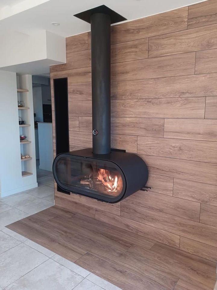 Cheminée moderne avec flammes ardentes, conduit noir, fixée sur un mur lambrissé.