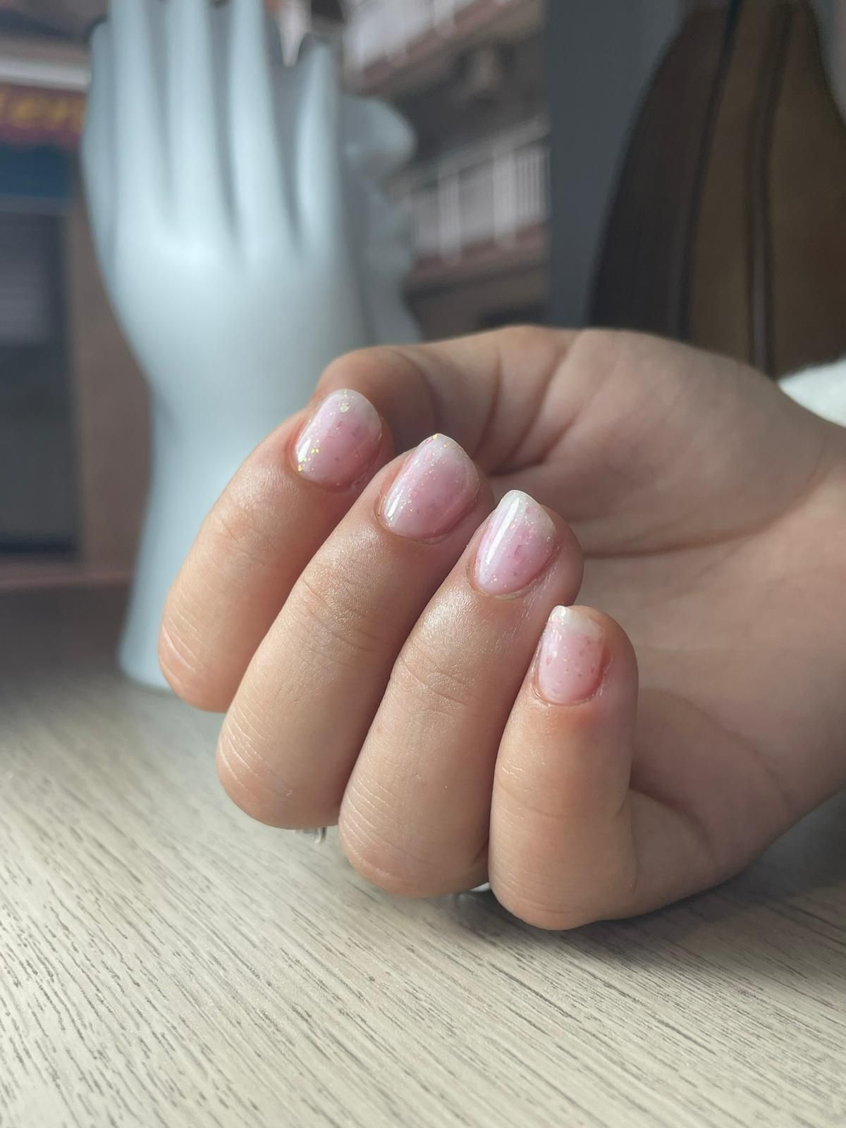 Mano con uñas cortas de aspecto natural, pintadas con un esmalte rosa claro brillante.