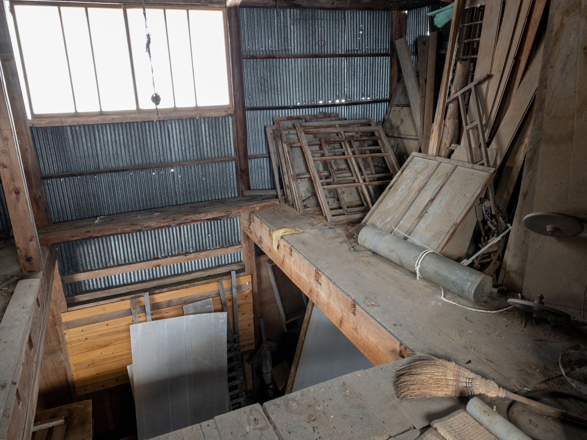 Vue intérieure d'un hangar en bois rustique et encombré, avec un mur en tôle ondulée, un espace en mezzanine