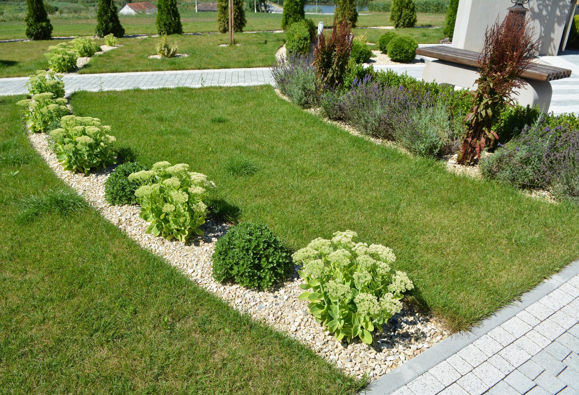 Jardin verdoyant et luxuriant avec des roches blanches, de l'herbe taillée et diverses plantes verte et violette.