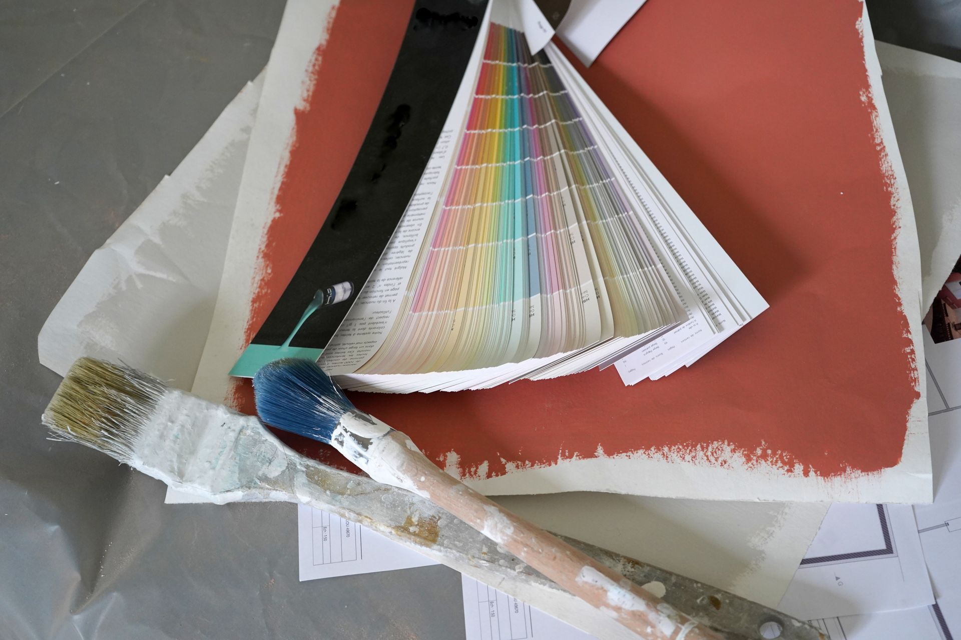 Échantillons de peinture, pinceaux et un éventail de couleurs sur une surface recouverte de papier.