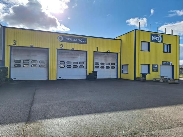 Bâtiment jaune avec trois portes de garage et une pancarte.