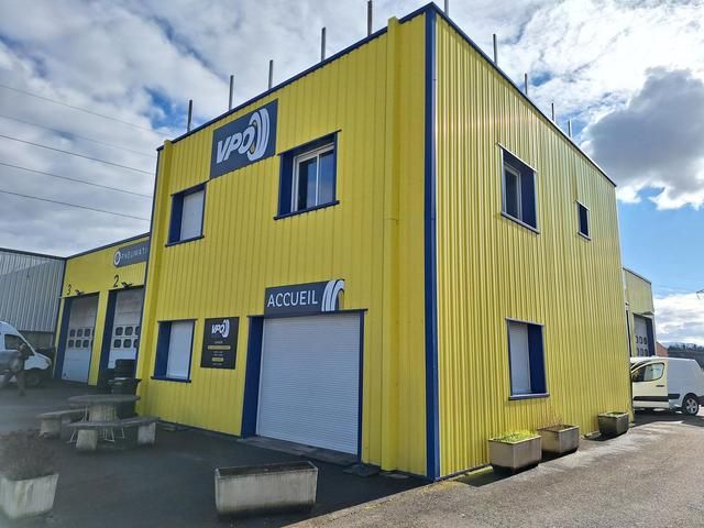 Bâtiment industriel jaune à bordures bleues, ciel nuageux.